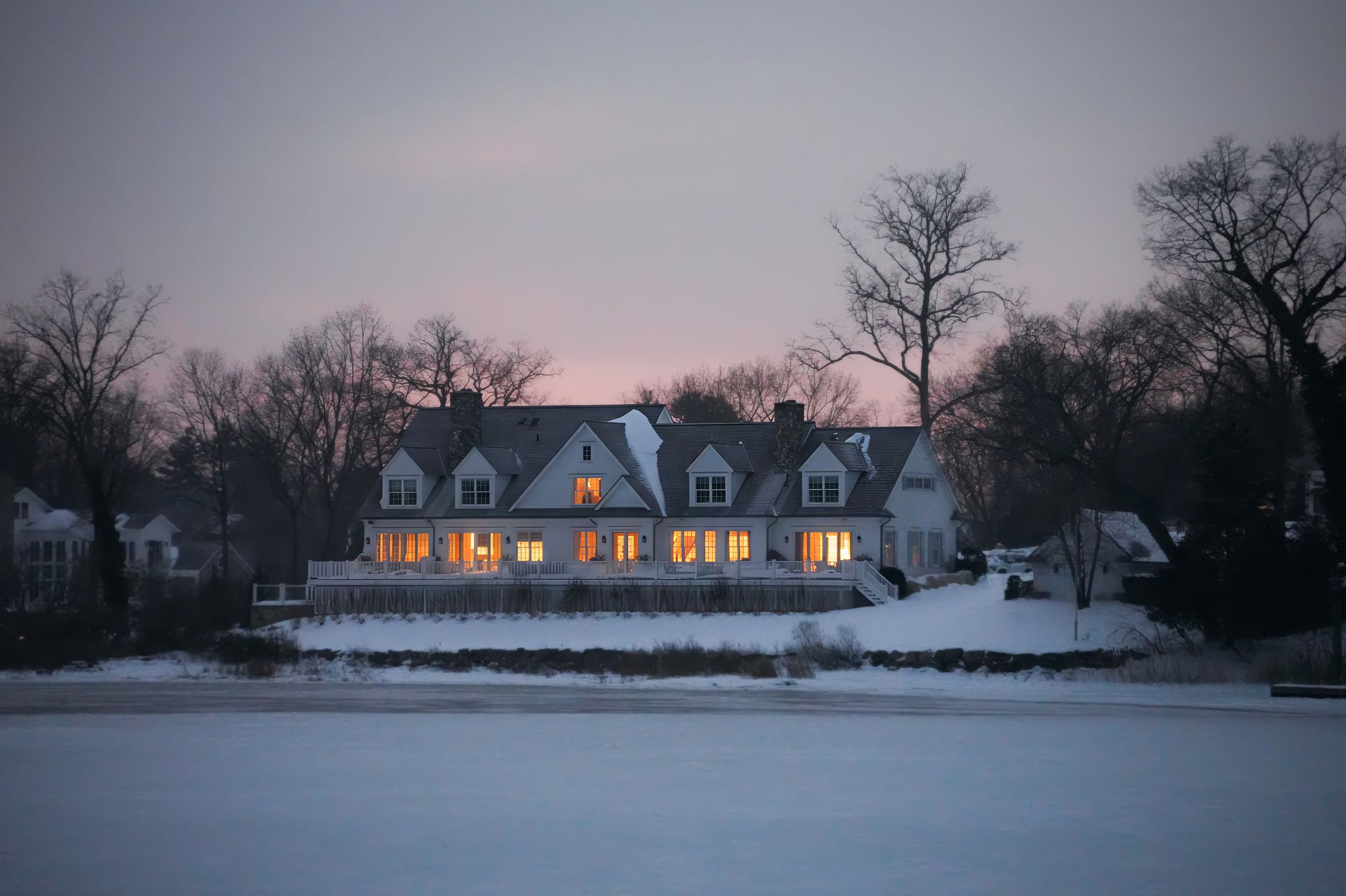 House at winter dusk with warm glowing windows over snow
