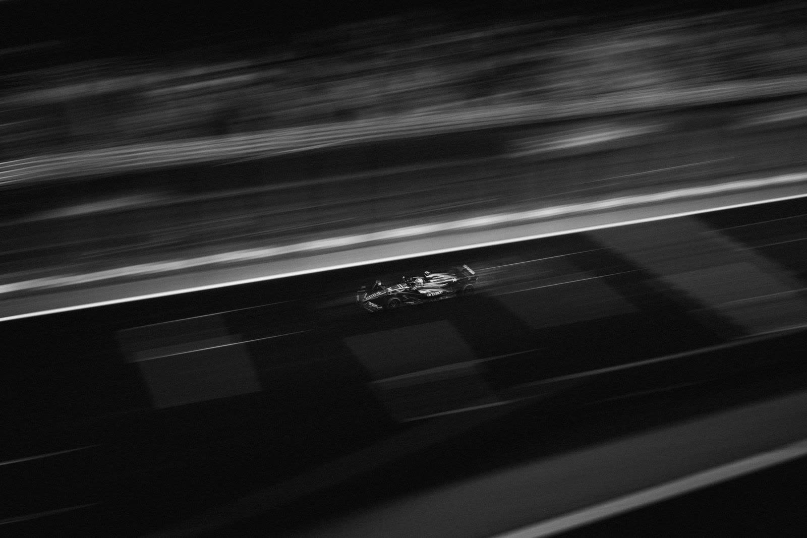 Open-wheel race car at speed under lights at night, motion-blurred