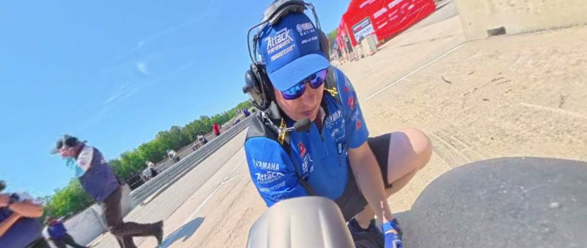 A mechanic in a headset kneels at a racebike in pit lane
